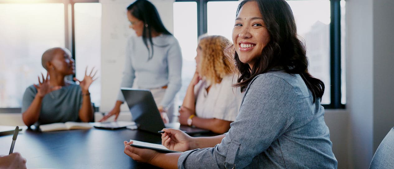 A smiling woman holding a tablet participates in an Intrapreneurship Academy course with colleagues.