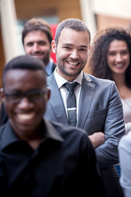 A diverse group of professionals smiling and standing in a line, with the focus on a man in a grey suit at the front.